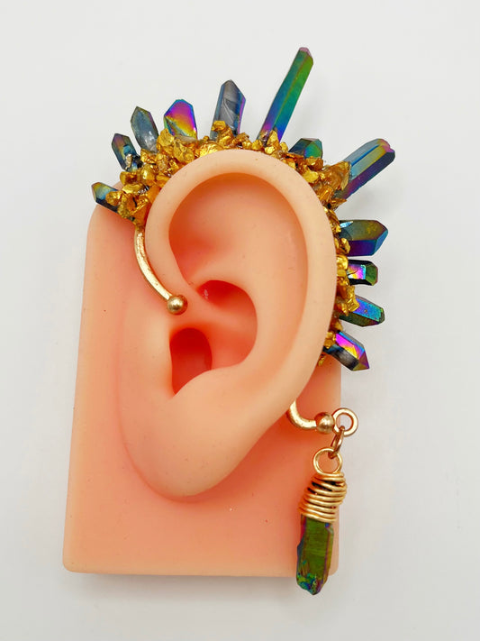 Blue rainbow titanium quartz crystal ear cuff with gold accents, modeled on an ear. A wire wrapped stone hangs from the bottom of the cuff behind the ear.