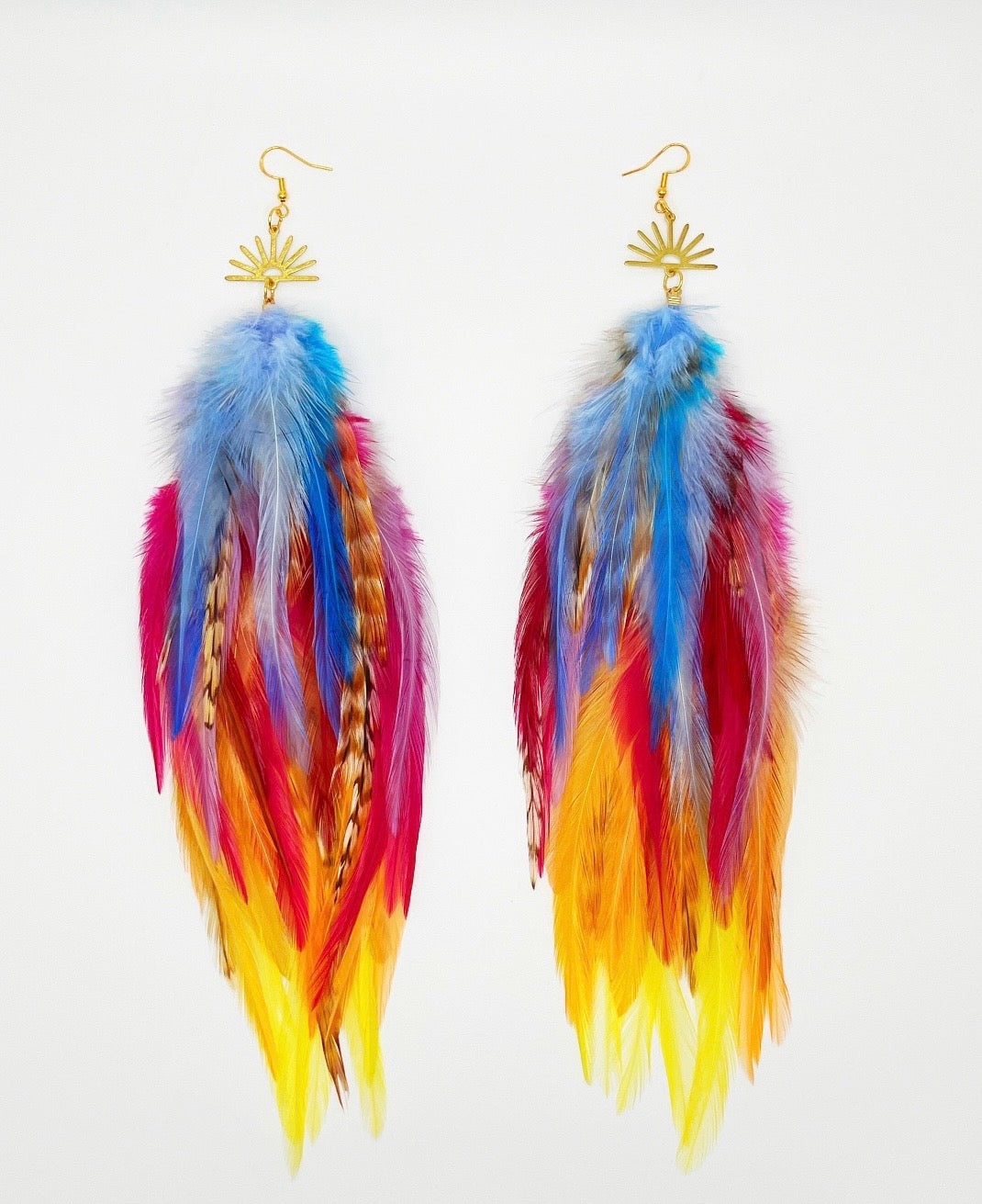 Vibrant bohemian feather earrings with blue, pink, orange and yellow feathers that hang from a gold sun pendant. 