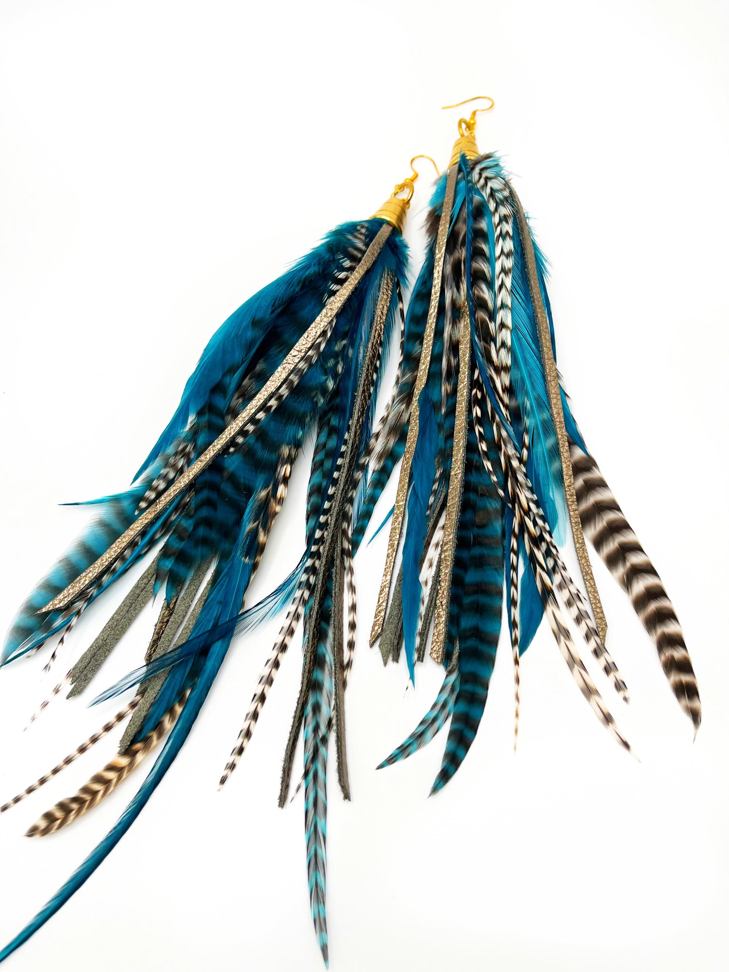 Long teal rooster feather earrings with strips of metallic bronze leather. Feathers and leather hang from under a gold colored pendant.