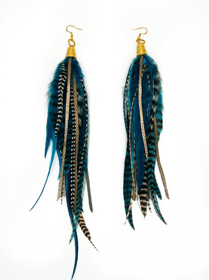 Long teal rooster feather earrings with strips of metallic bronze leather. Feathers and leather hang from under a gold colored pendant. 