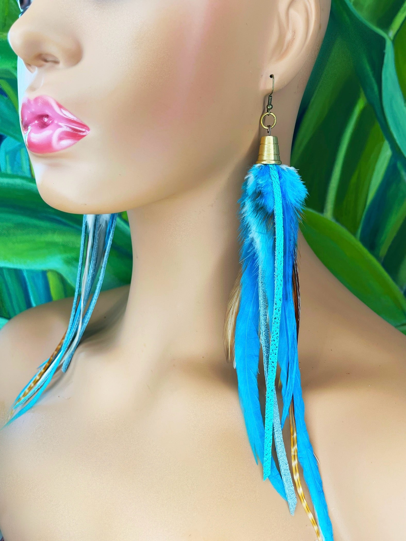 A mannequin wearing long turquoise blue feather earrings with strips of metallic leather, hanging from a gold colored cap pendant.