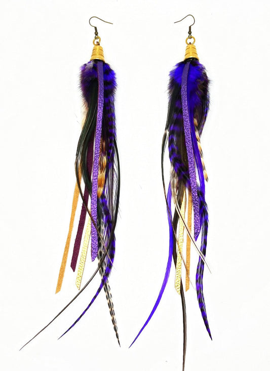 Long feather earrings in dark purple and natural tones, with metallic purple and gold leather strips, hanging from a gold colored cap pendant.