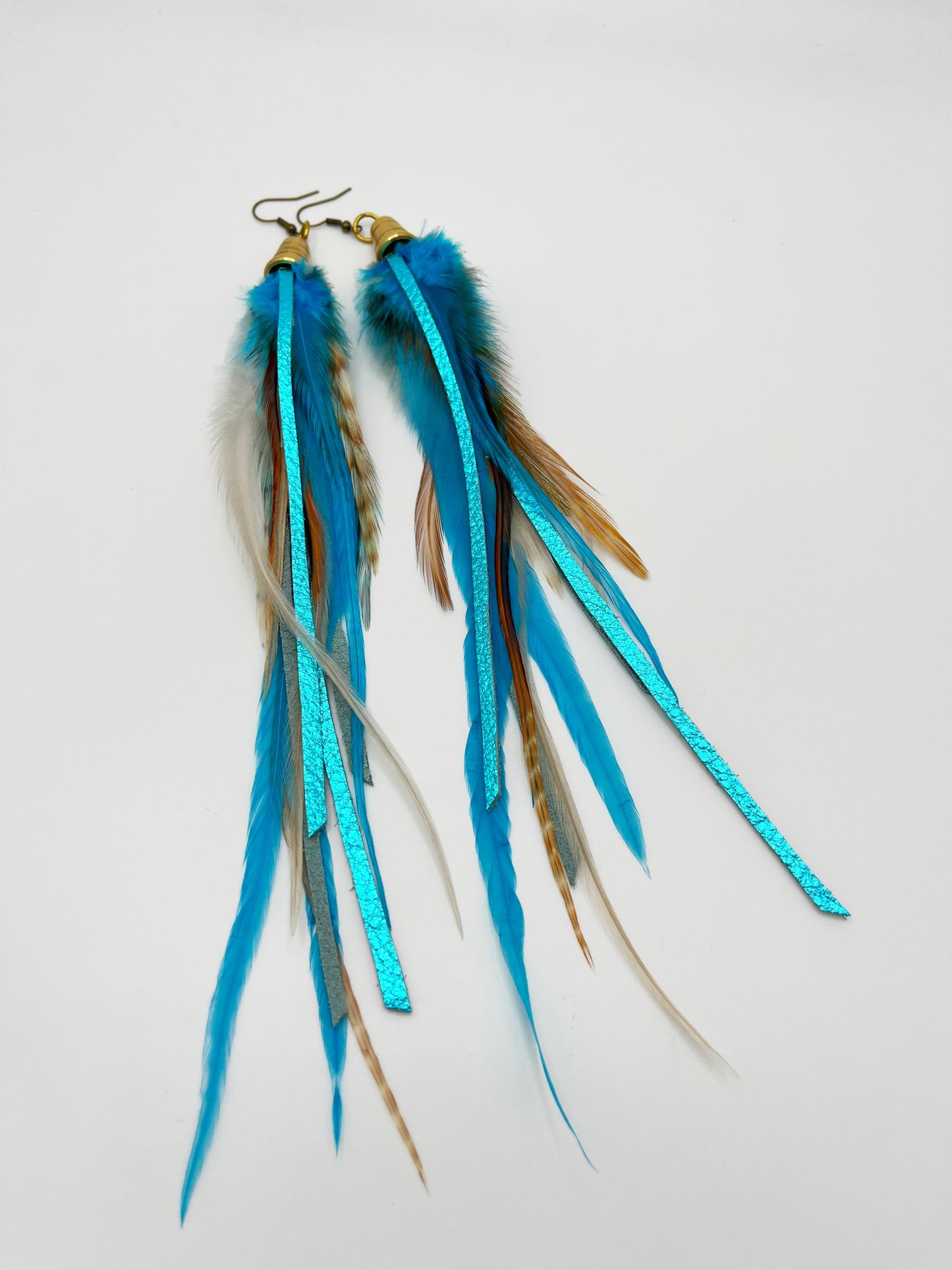 Long turquoise blue feather earrings with strips of metallic leather, hanging from a gold colored cap pendant.