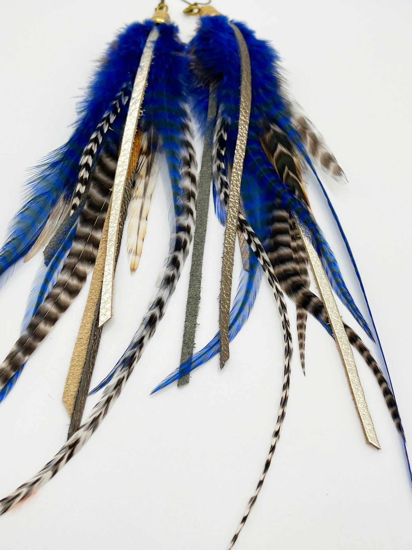 Long feather earrings in dark blue and natural colors, with strips of metallic pewter and bronze leather, hanging from a gold colored cap pendant.