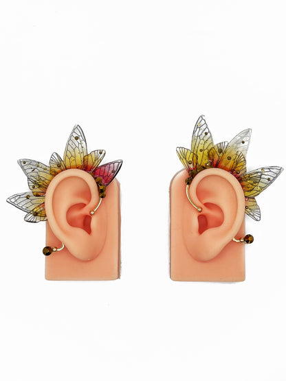 Yellow and red fairy wing ear cuffs with gold rhinestones, modeled on a pair of ears. 