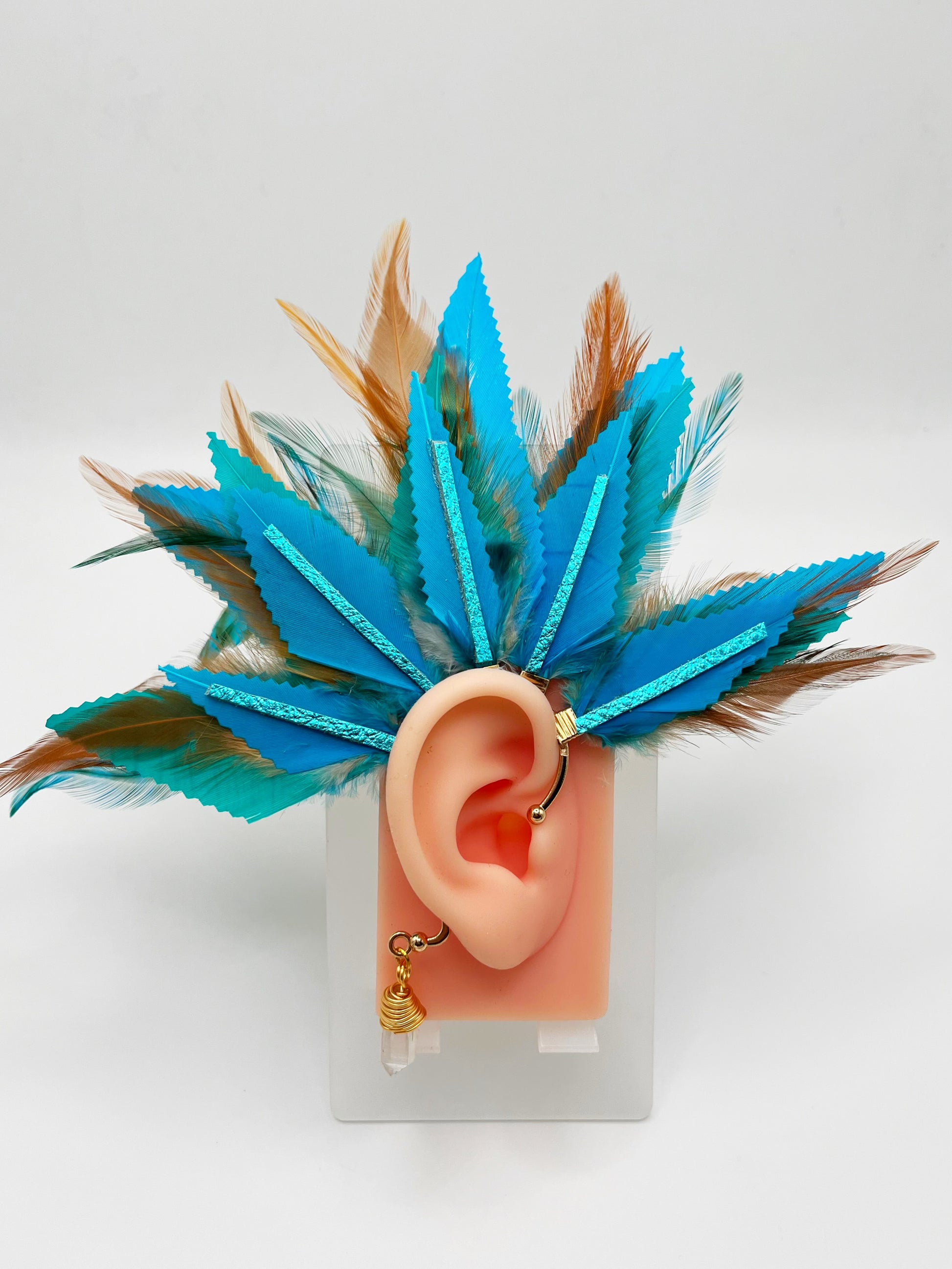 Turquoise blue and light brown feather ear cuff with blue leather accents and wire wrapped quartz dangle, modeled on an ear. 