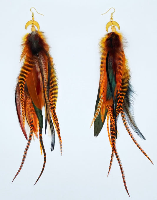 Long brown and orange feather earrings with warm tones, hanging from gold crescent moon pendants. 