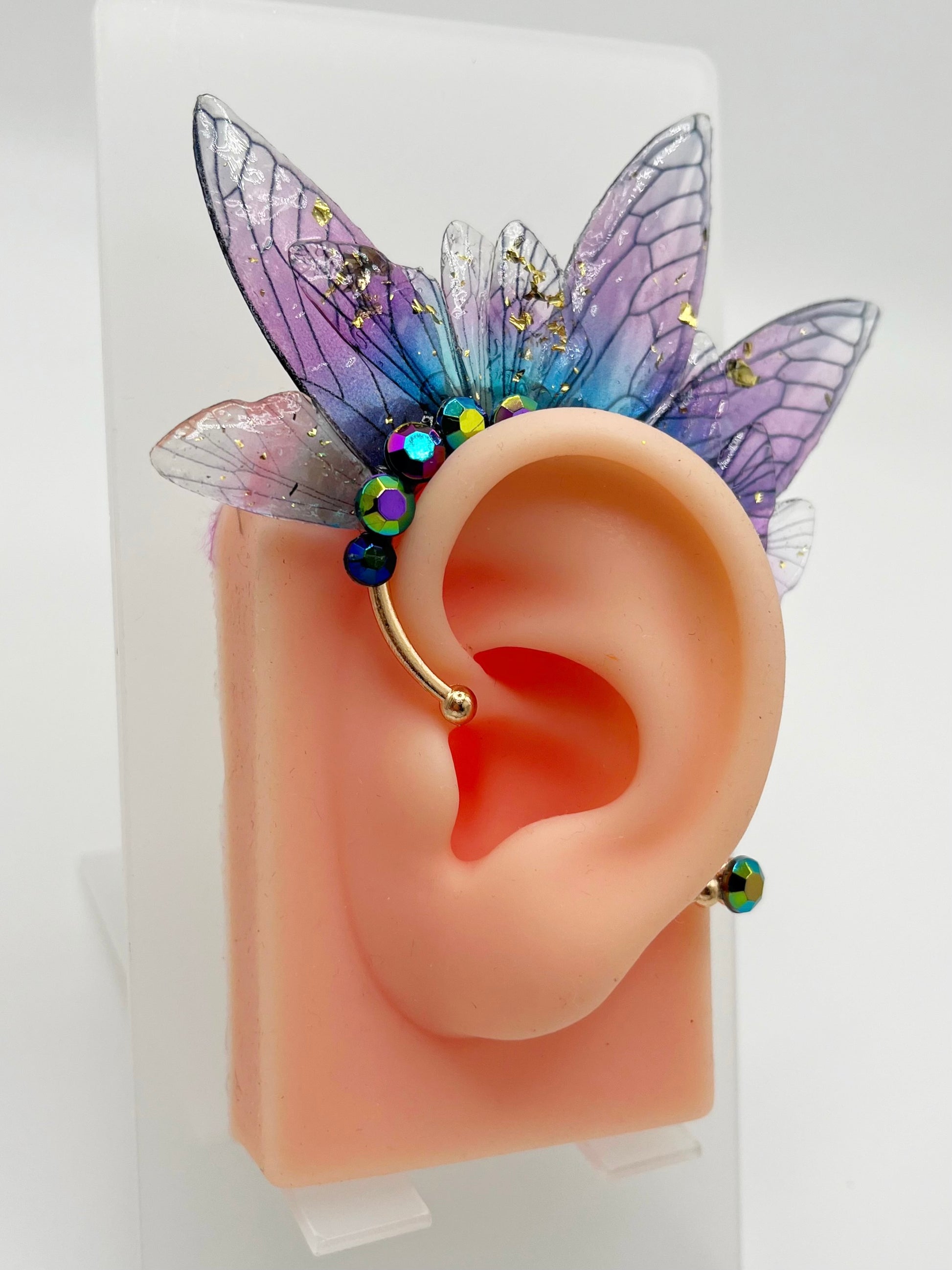Purple fairy wing ear cuff with blue rhinestones, modeled on an ear.