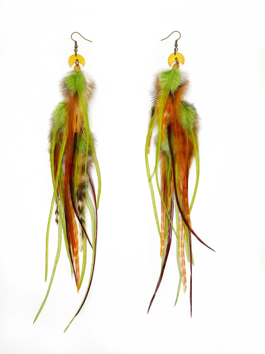 long rooster feather earrings in brown and pistachio green tones, hanging from gold crescent moon pendants.