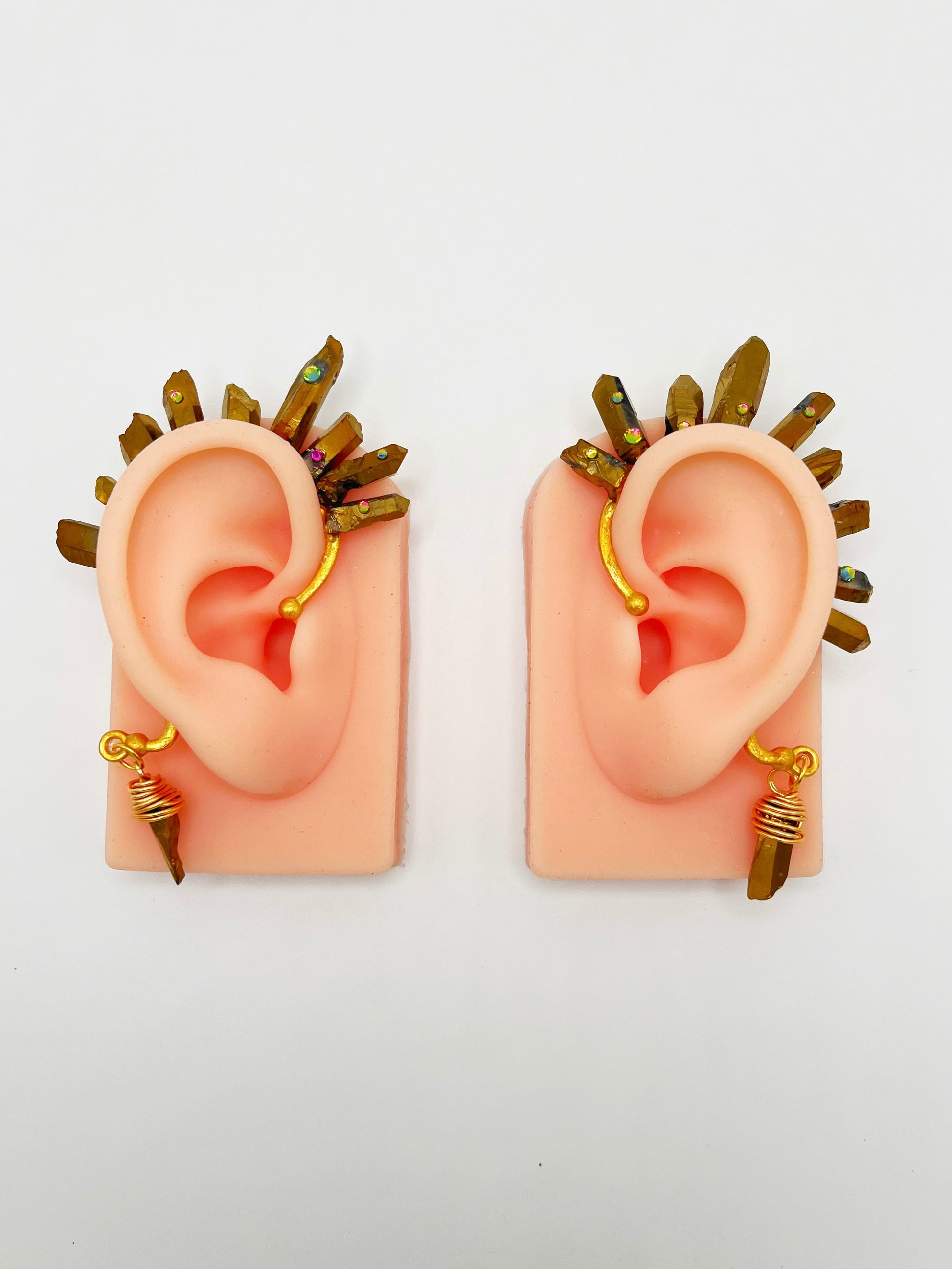 Gold pyrite quartz crystal ear cuffs with rhinestones, modeled on a pair of ears. A wire wrapped stone hangs from the bottom of the cuff behind the ear.