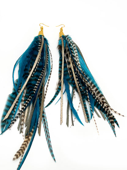 Long teal rooster feather earrings with strips of metallic bronze leather. Feathers and leather hang from under a gold colored pendant.