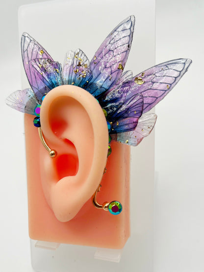 Purple fairy wing ear cuff with blue rhinestone, modeled on an ear.