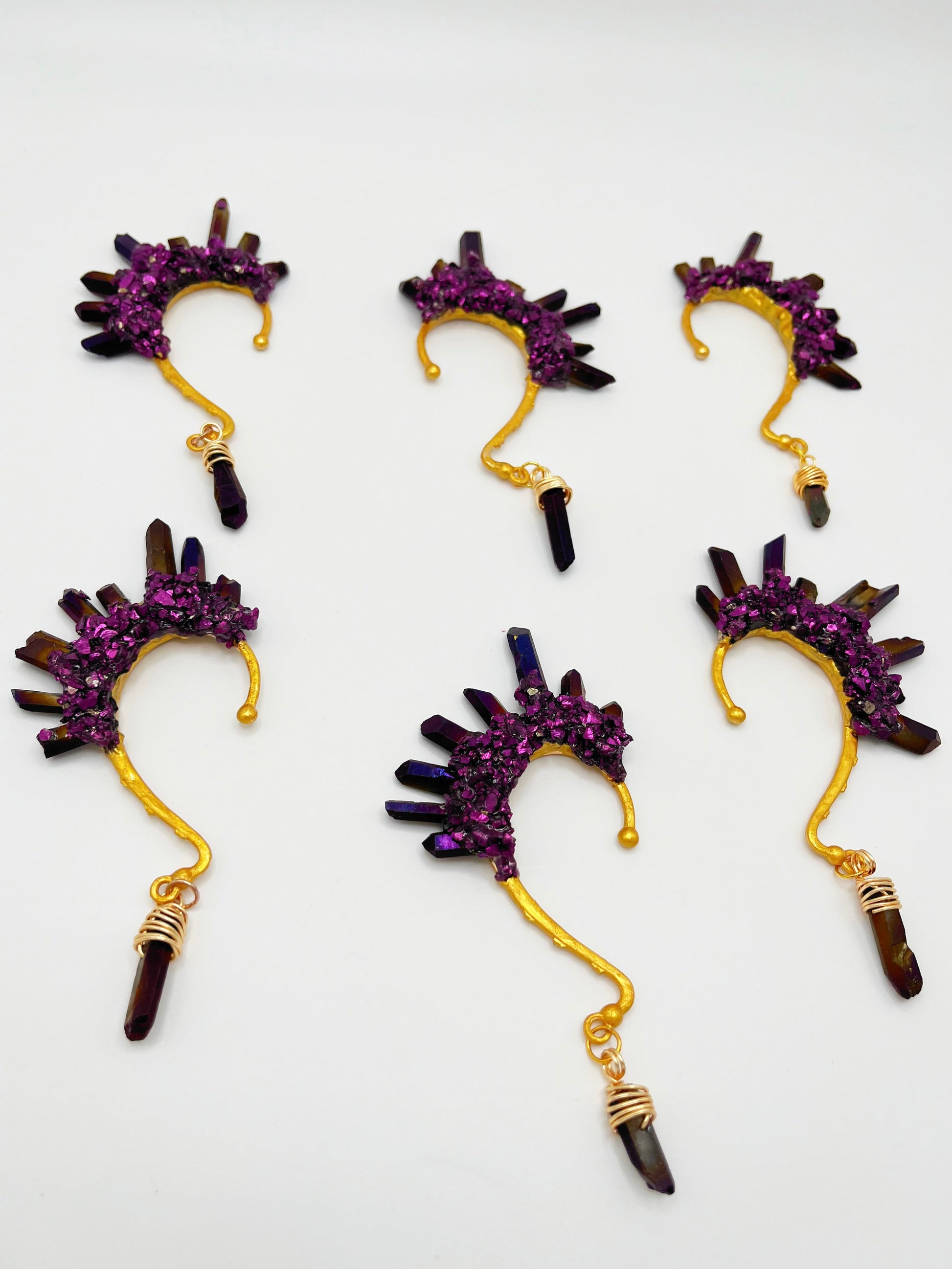 Six purple titanium coated quartz ear cuffs with a wire wrapped stone hanging from the bottom of each cuff. Each cuff is gold toned.