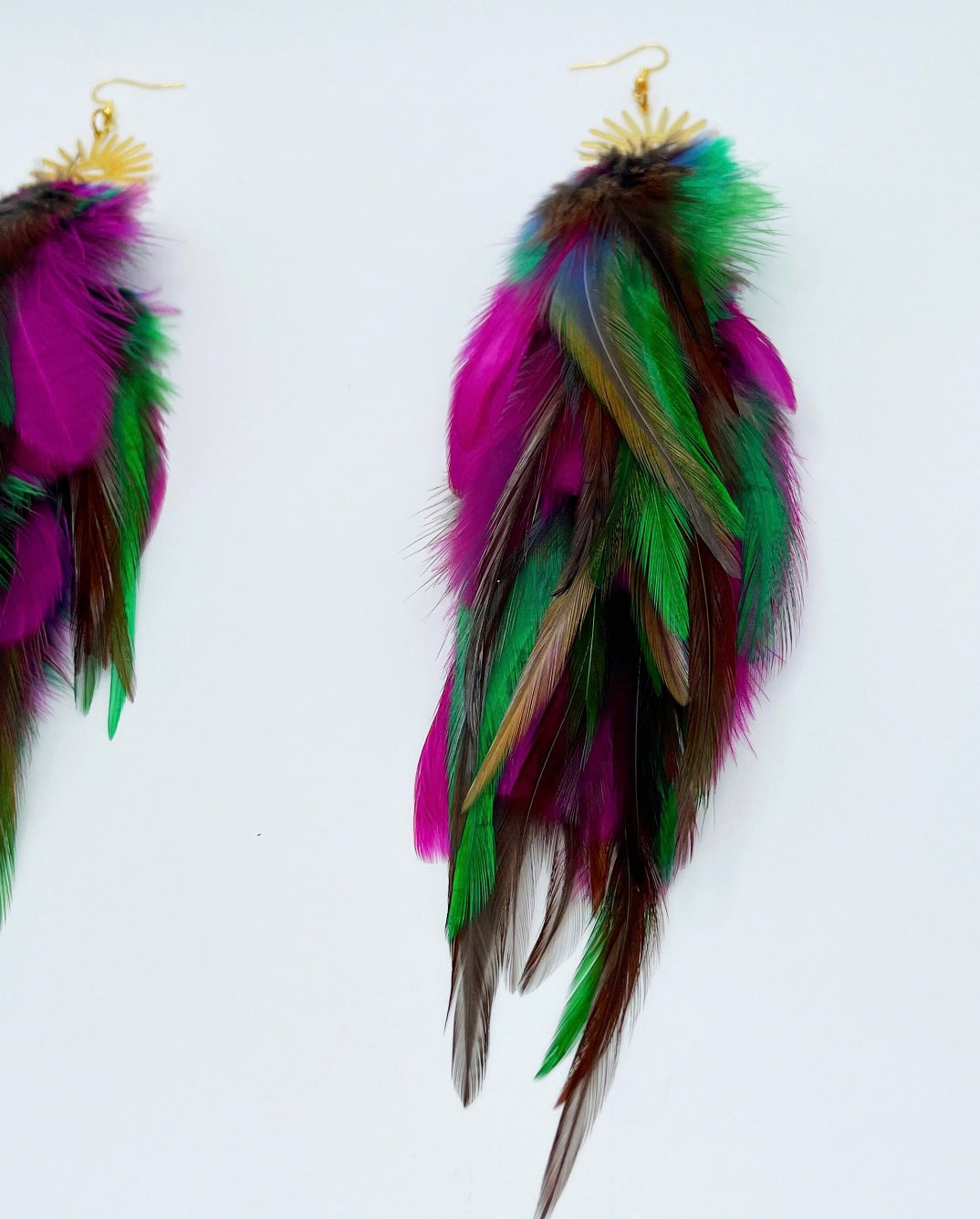 Colorful long feather earrings with gold sunburst pendants, featuring hues of purple, green, and pink against a white background, ideal for boho chic fashion.