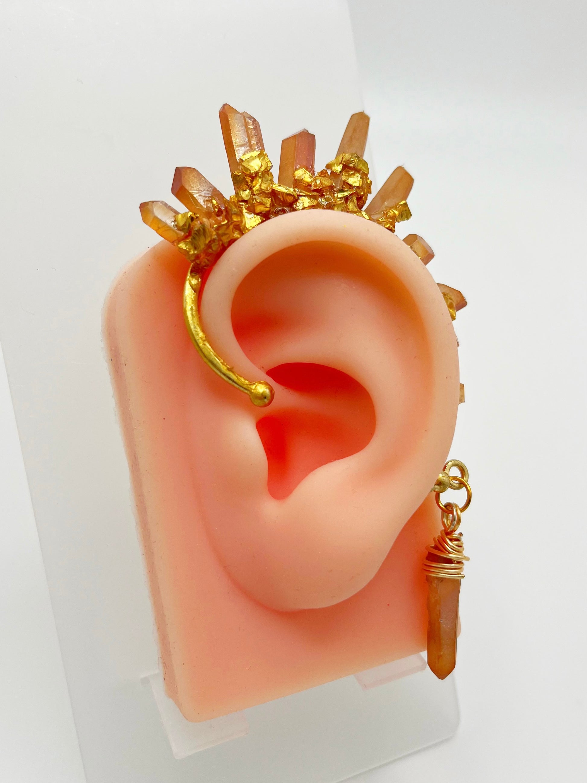 Orange citrine crystal ear cuff with crushed gold accents, modeled on an ear. A wire wrapped stone hangs from the bottom of the cuff behind the ear.