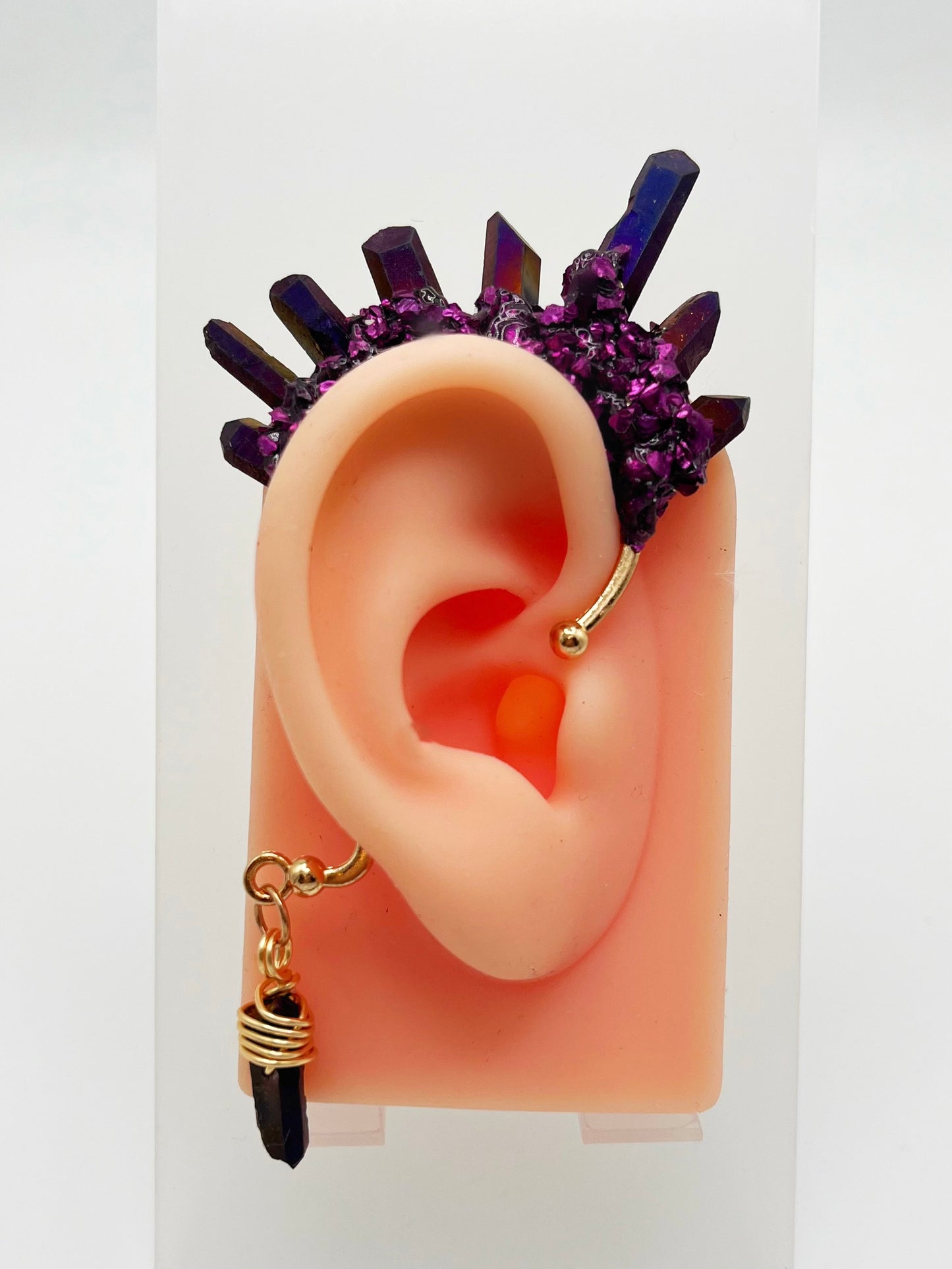 Purple titanium quartz ear cuff with purple metallic accents, modeled on an ear. A wire wrapped quartz hangs from the bottom of the cuff behind the ear.