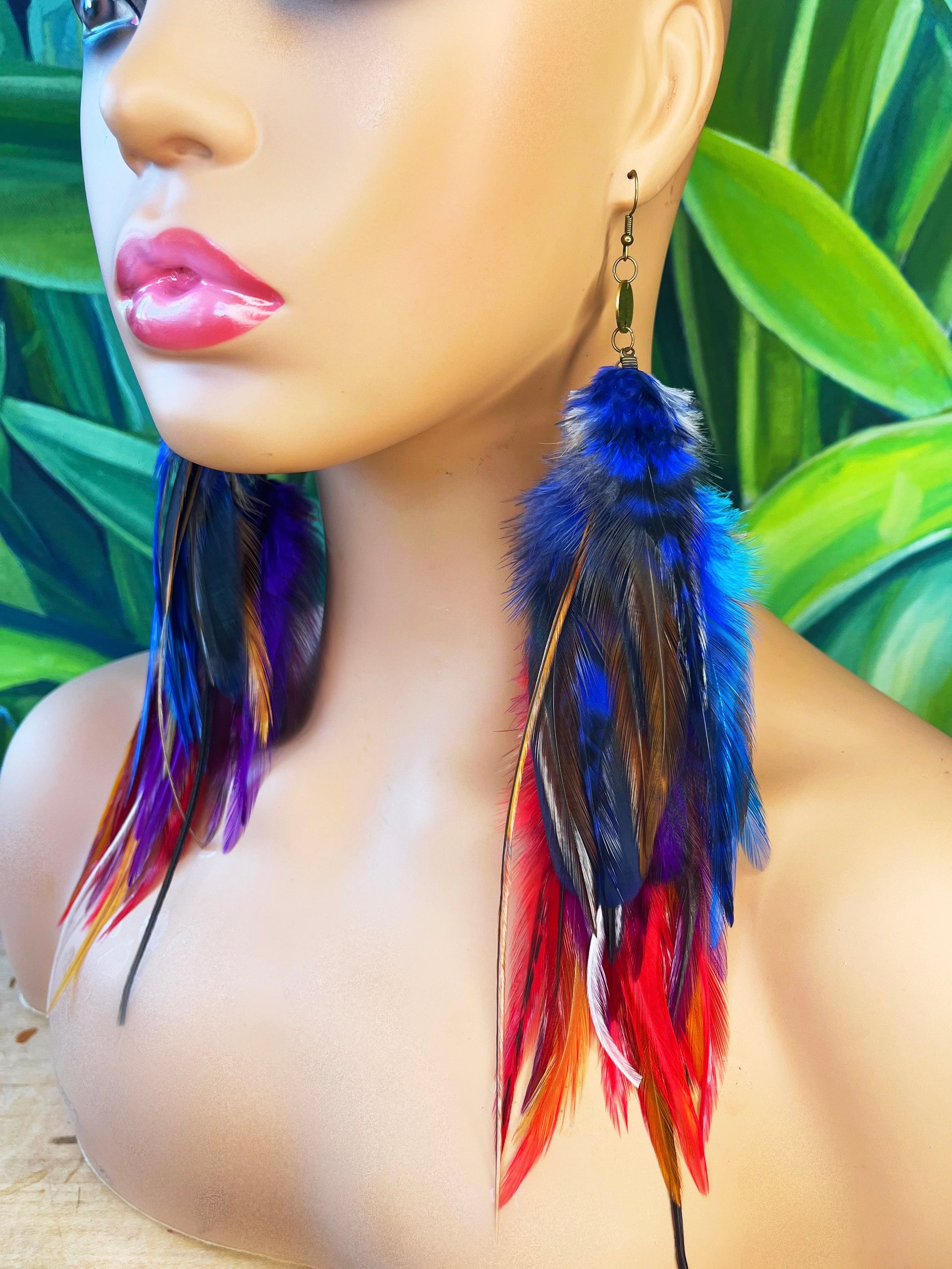 Vibrant long feather earrings displayed on a mannequin, showcasing bold colors of blue, purple, and red against a tropical background, ideal for statement-making bohemian style.