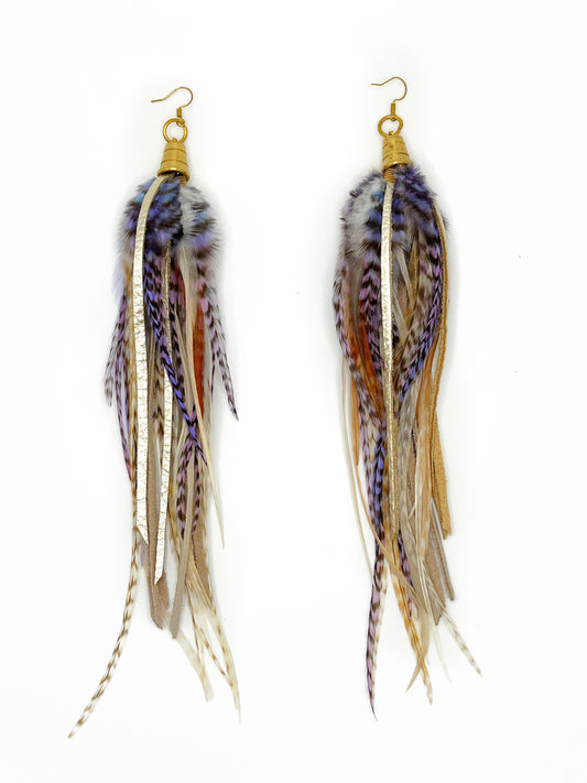 Long feather earrings in beige, pink, purple and lavender tones with strips of metallic pewter leather. All leather and feathers hang from under a gold colored bead cap.