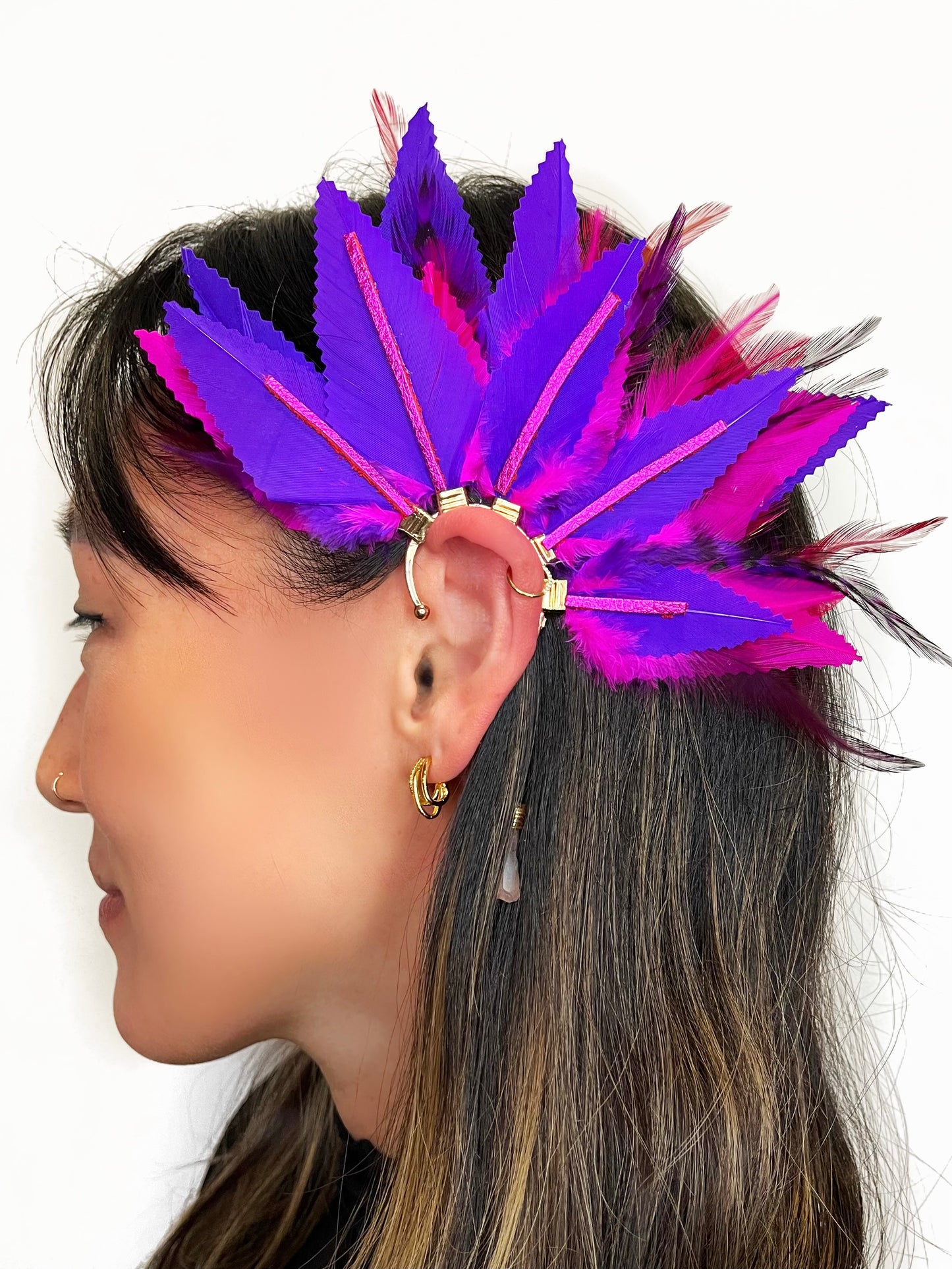 Woman wearing a structured feather ear cuff in vibrant purple and pink colors, worn on the left ear. 