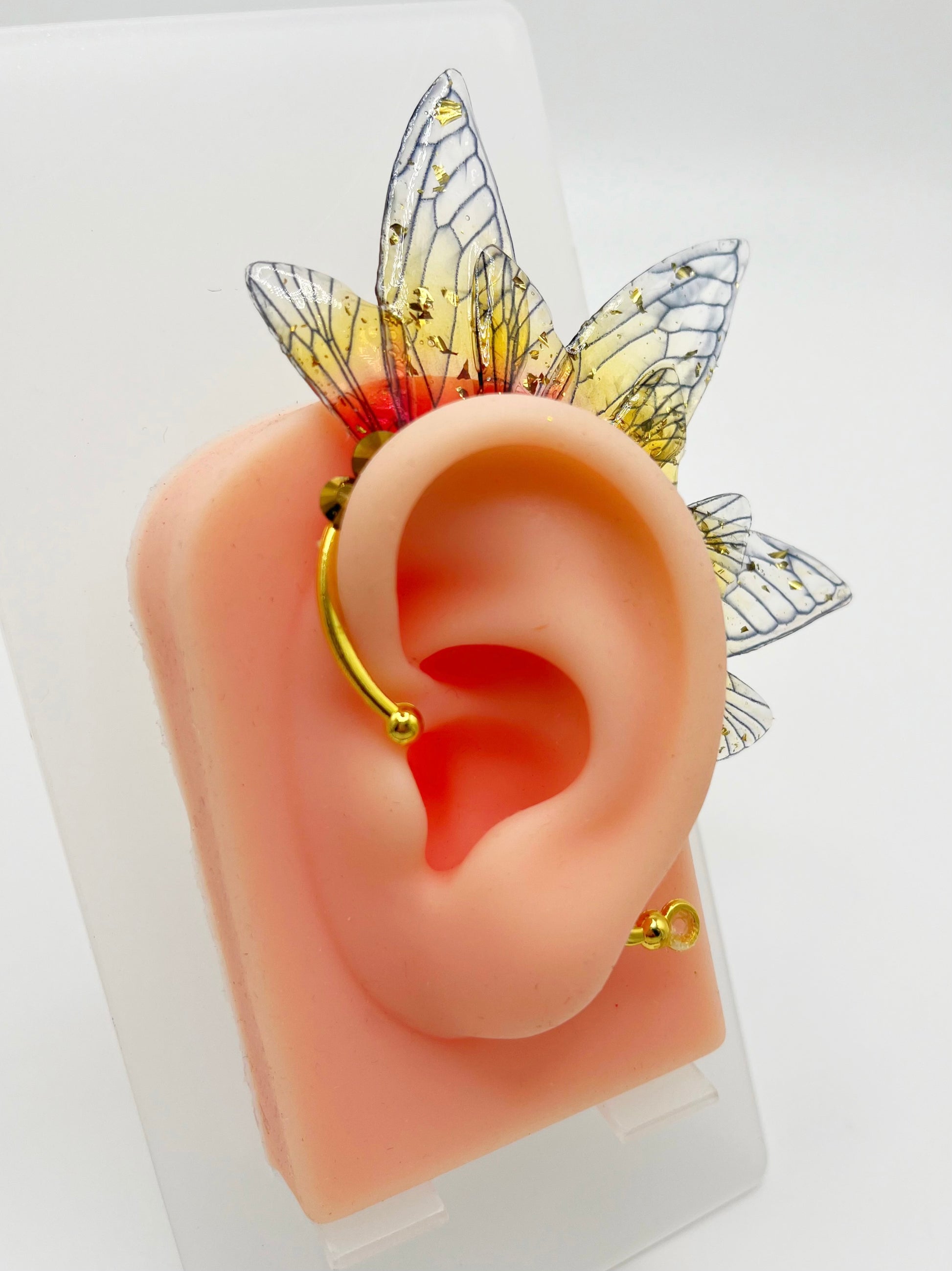 Yellow and red fairy wing ear cuff with gold rhinestones, modeled on an ear.