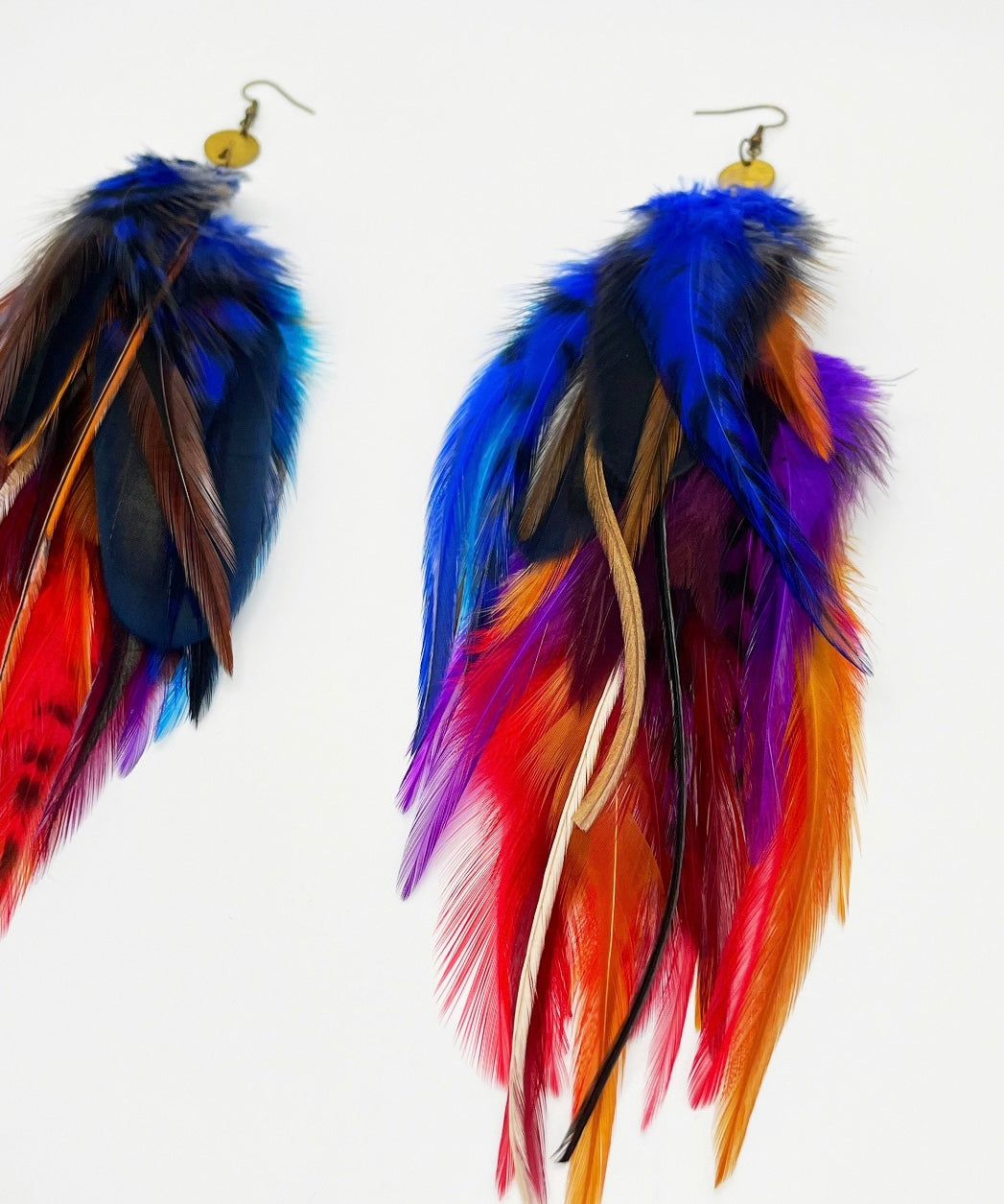  A pair of handcrafted long feather earrings with vibrant hues of red, blue, yellow, and purple, featuring a gold-colored bronze circular pendant and hypoallergenic ear wire, perfect for bohemian and festival-inspired fashion.