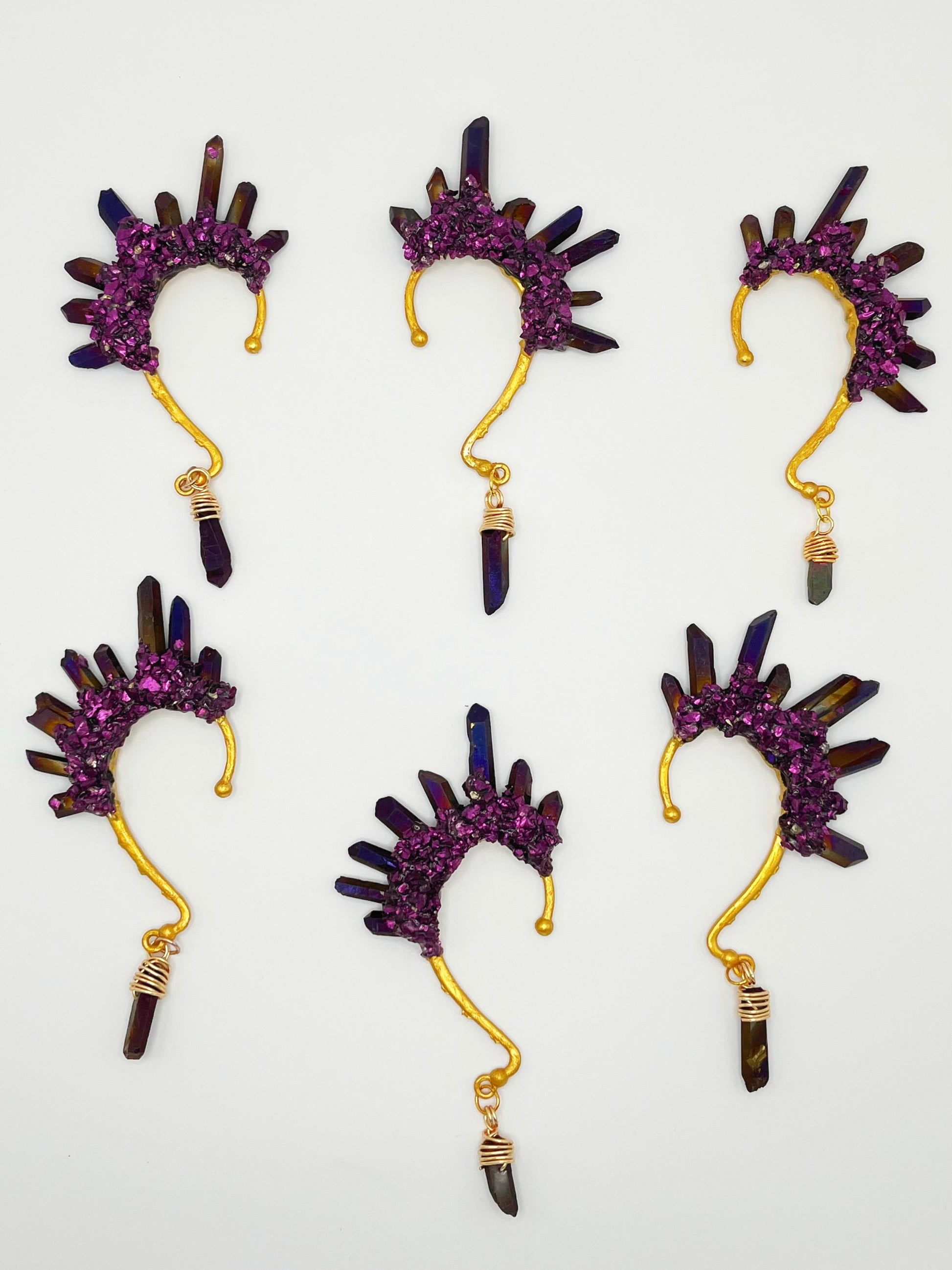 Six purple titanium coated quartz ear cuffs with a wire wrapped stone hanging from the bottom of each cuff. Each cuff is gold toned.