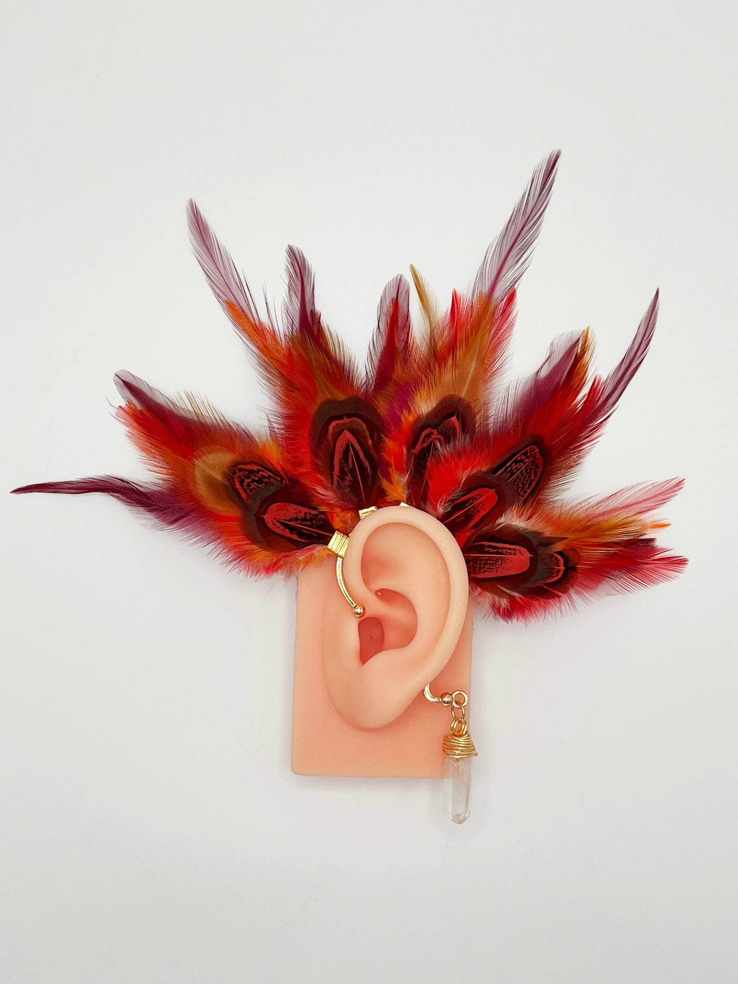 Rooster and pheasant ear cuff in vibrant red and orange colors, modeled on an ear. A wire wrapped quartz stone dangles from the bottom of the cuff behind the ear.