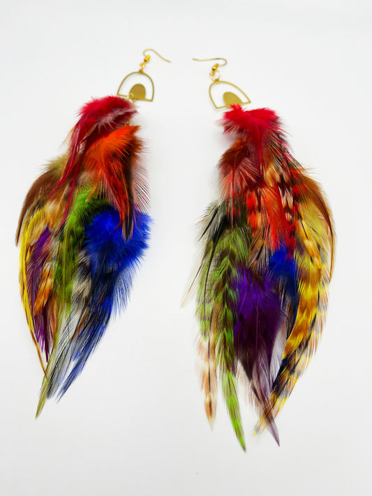 Long bohemian feather earrings in rainbow colors, hanging from a gold rainbow pendant. 