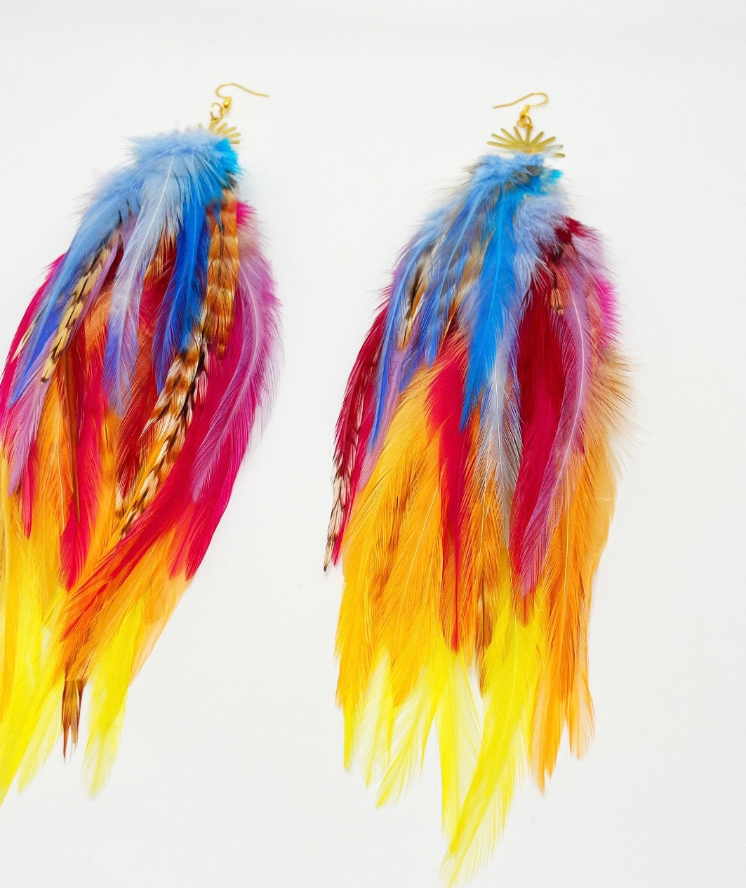 Vibrant bohemian feather earrings with blue, pink, orange and yellow feathers that hang from a gold sun pendant.