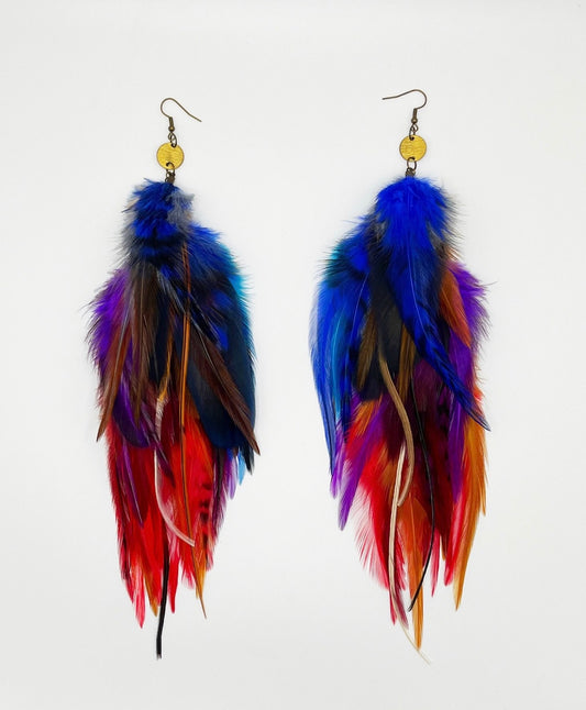  A pair of handcrafted long feather earrings with vibrant hues of red, blue, yellow, and purple, featuring a gold-colored bronze circular pendant and hypoallergenic ear wire, perfect for bohemian and festival-inspired fashion.