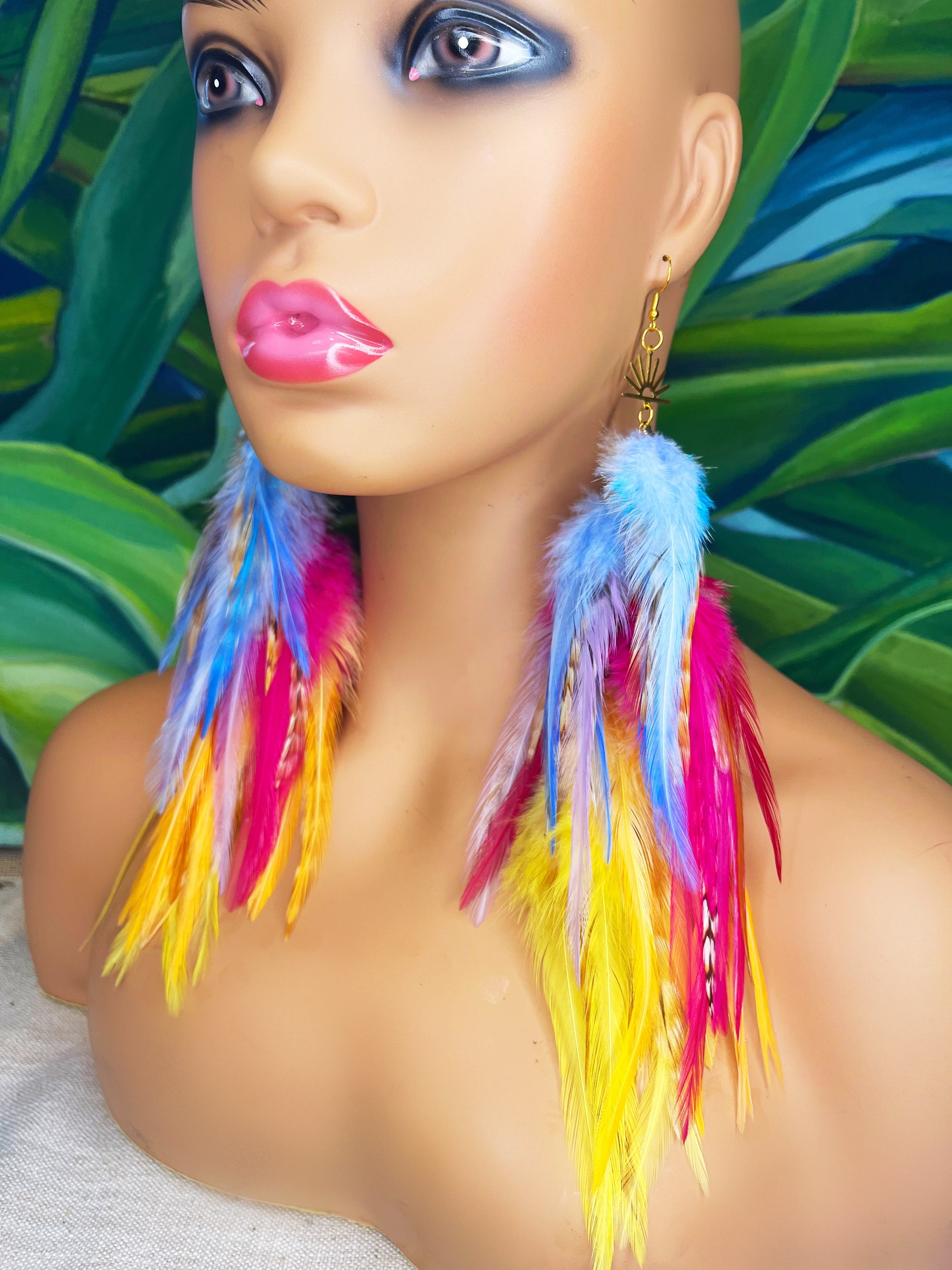 Mannequin wearing vibrant bohemian feather earrings with blue, pink, orange and yellow feathers that hang from a gold sun pendant.