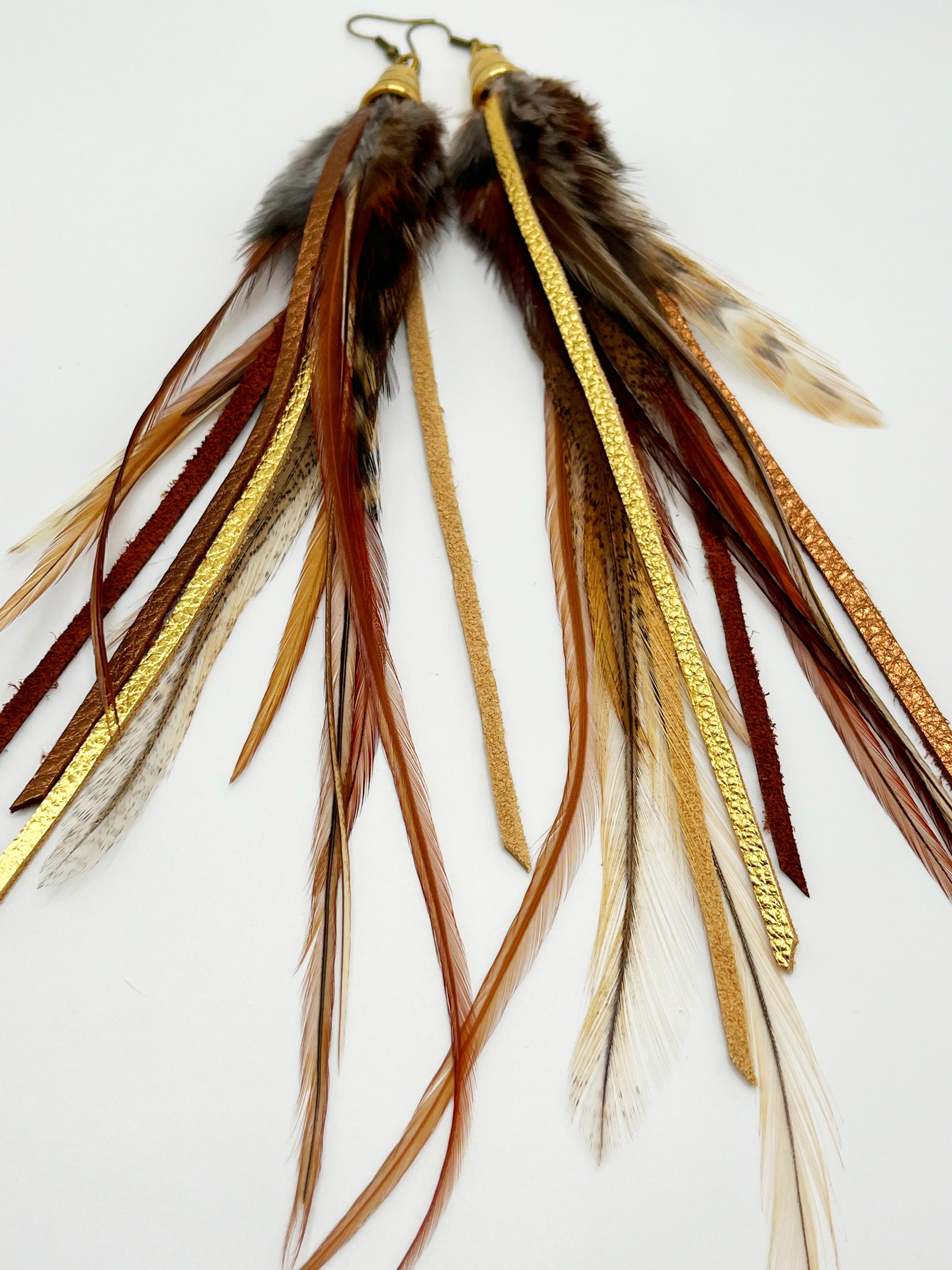 Dark brown feather earrings with metallic gold and bronze leather strips, hanging from a gold colored cap pendant.