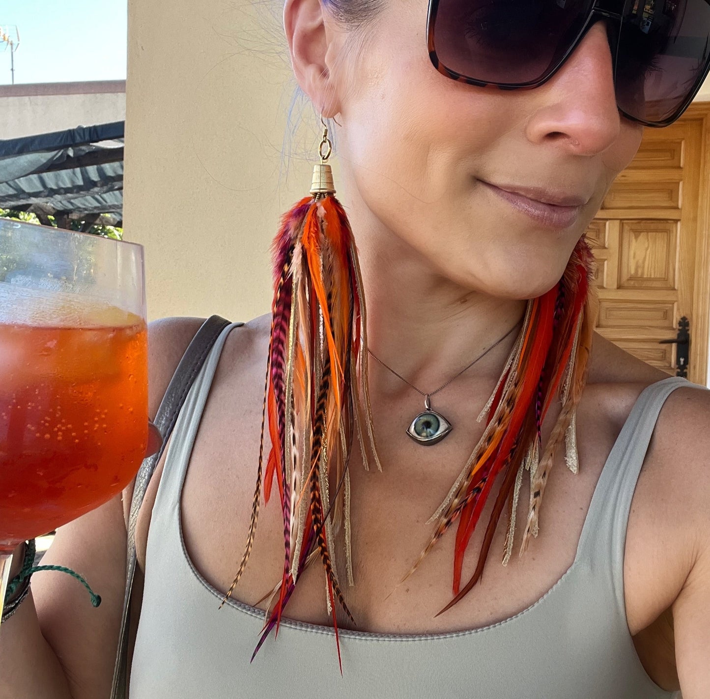 Woman wearing long feather earrings in vibrant orange tones.