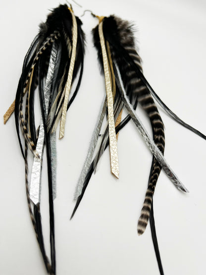 Long black and white feather earrings, with metallic silver and pewter colored leather strips, hanging from a gold colored cap pendant.