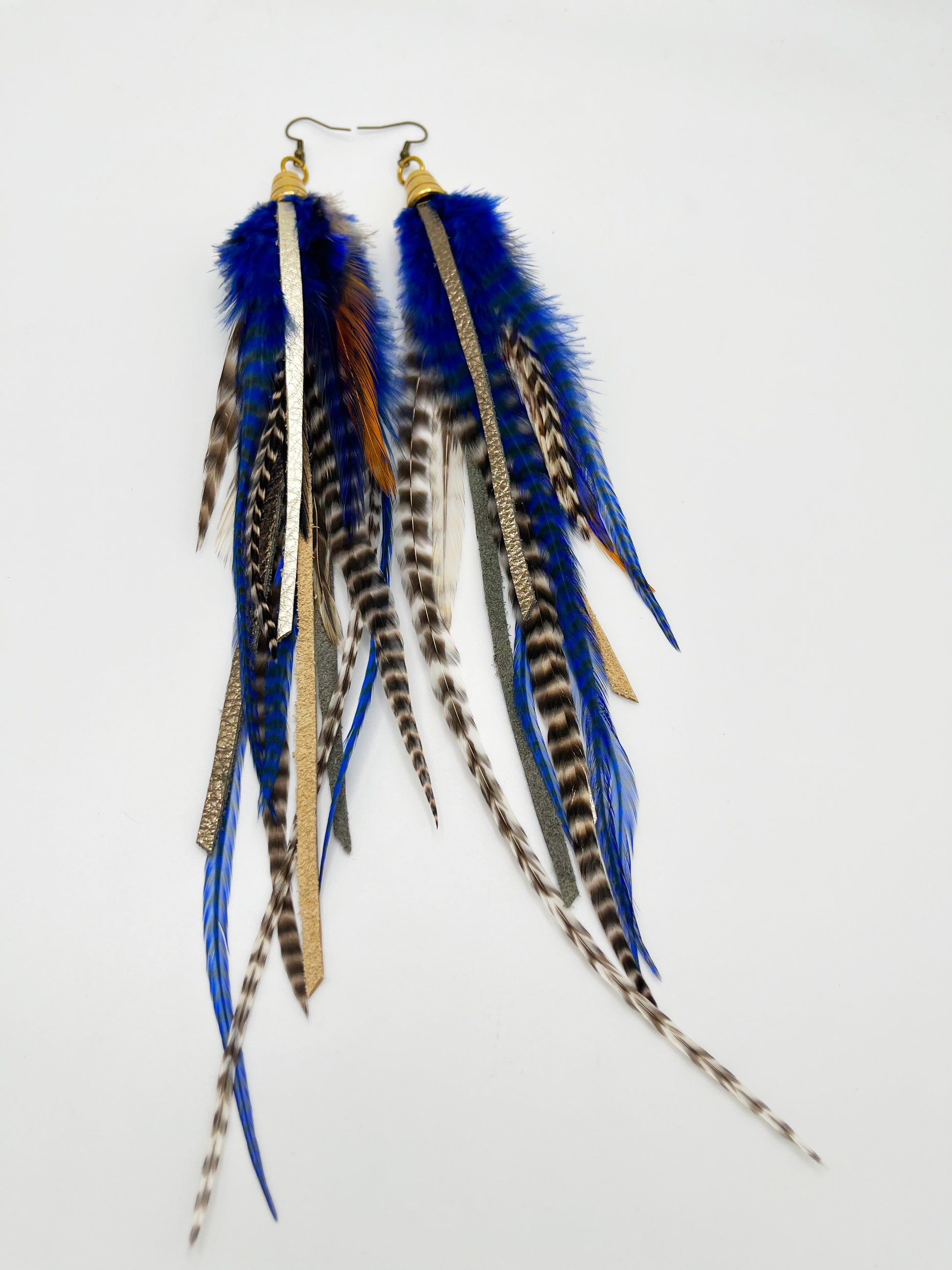 Long feather earrings in dark blue and natural colors, with strips of metallic pewter and bronze leather, hanging from a gold colored cap pendant.