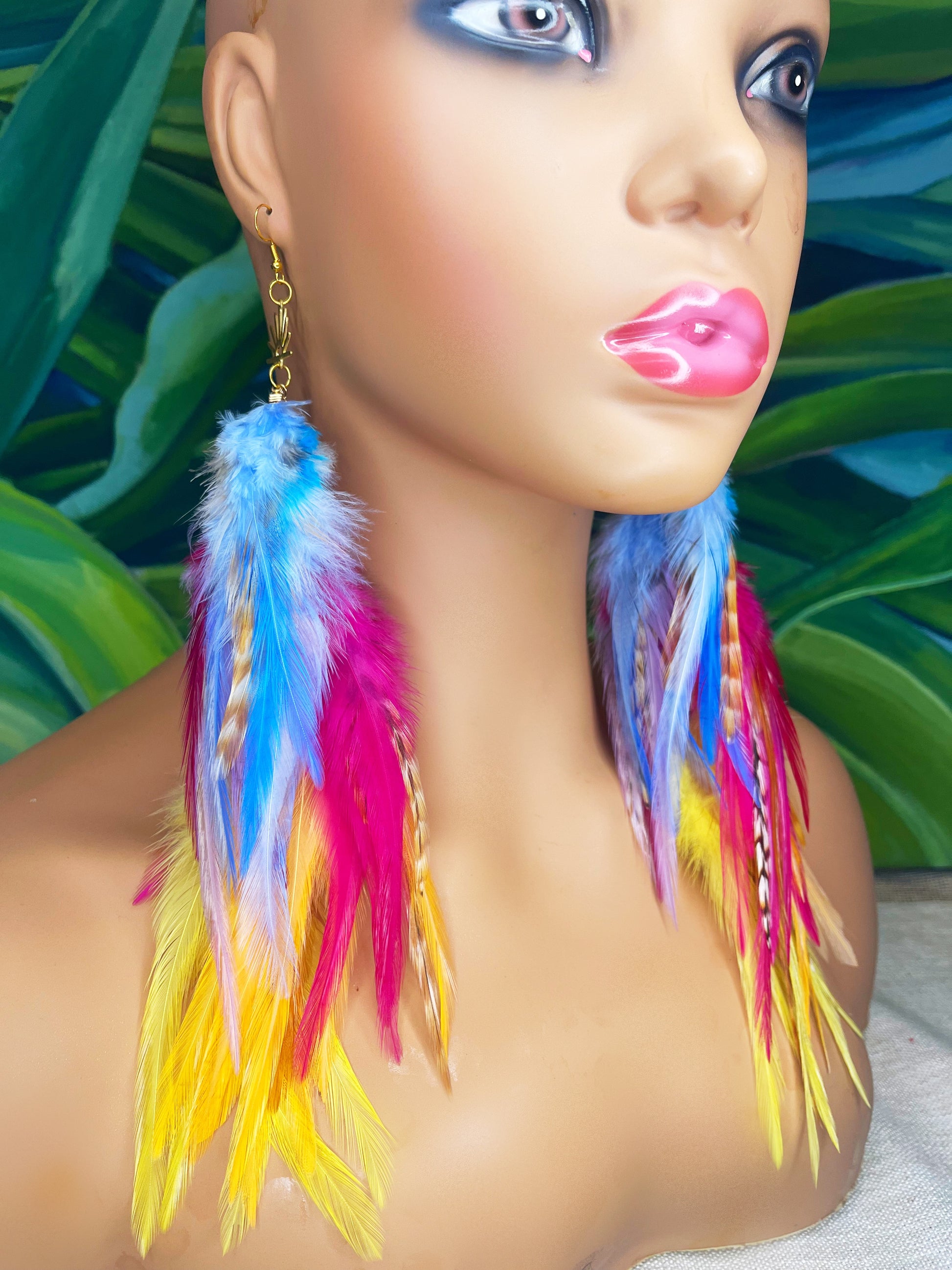 Mannequin wearing vibrant bohemian feather earrings with blue, pink, orange and yellow feathers that hang from a gold sun pendant.