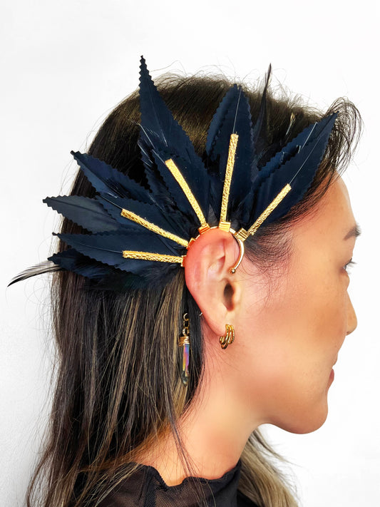 Structured black feather ear cuff with gold leather accents, modeled on a women. A wire wrapped quartz dangle hangs from the cuff behind the ear. 