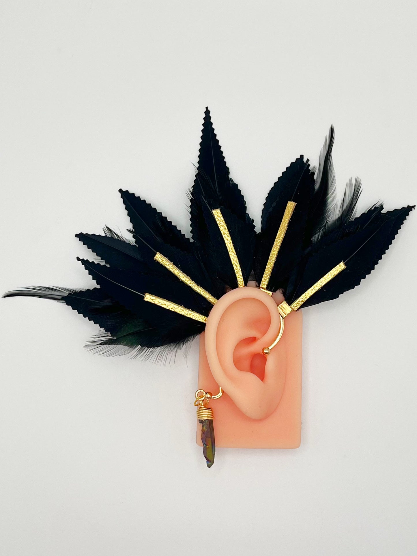 Structured black feather ear cuff with gold leather accents modeled on an ear. A black wire wrapped quartz hangs from the cuff behind the ear.