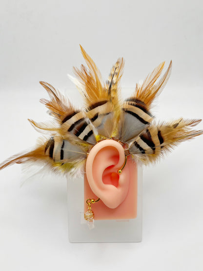 Rooster and chukar partridge feather ear cuff in white, cream, yellow and beige tones, modeled on an ear. A wire wrapped quartz stone hangs from the bottom of the cuff behind the ear.