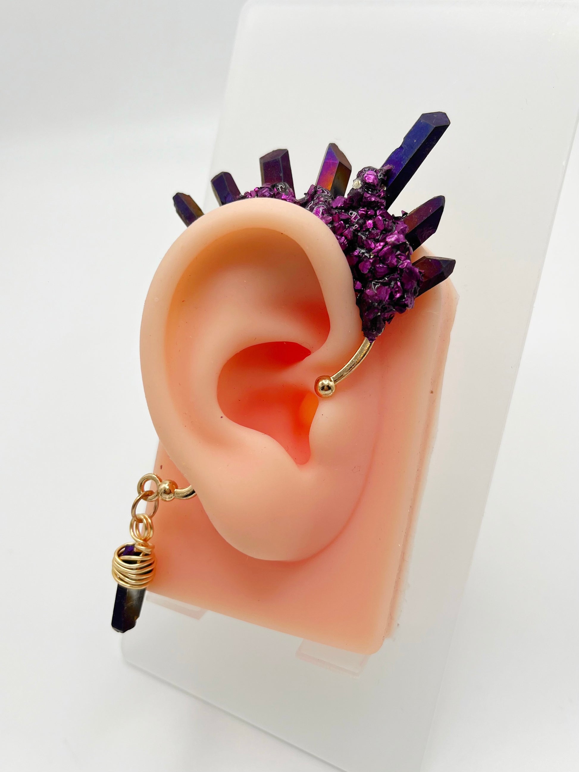 Purple titanium coated quartz ear cuff with metallic purple accents, modeled on an ear. A wire wrapped quartz stone is attached to the bottom of the cuff that hangs behind the ear.