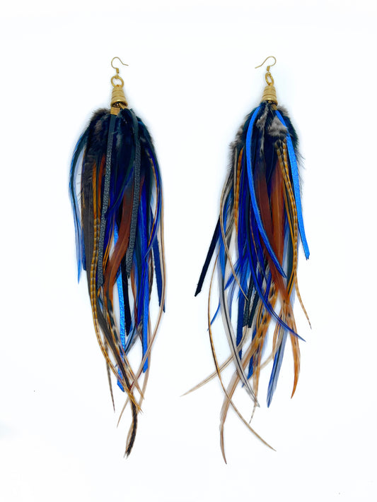 Long feather and leather earrings in dark blue and brown tones. All feathers hang from underneath a gold cap pendant. 