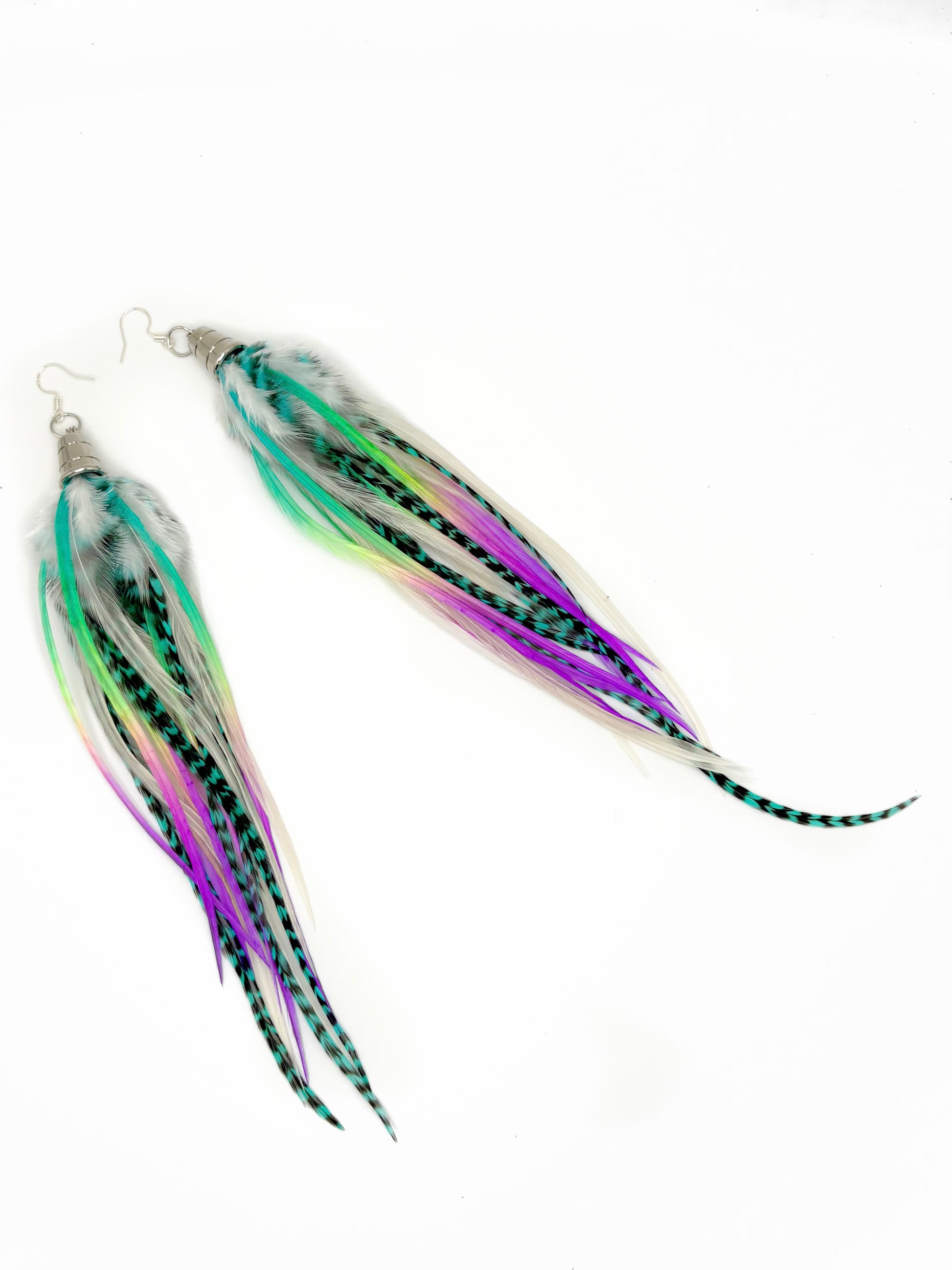 A pair of dangling feather earrings with long, thin feathers in white, black, green, purple, and pink, attached to silver fishhook wires, shown on a plain white background.