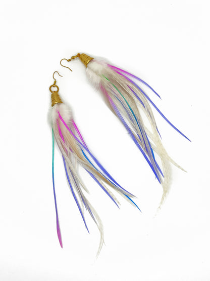 Long white feather earrings with pastel purple and pink accents. All feathers hang from beneath a gold cap pendant. 